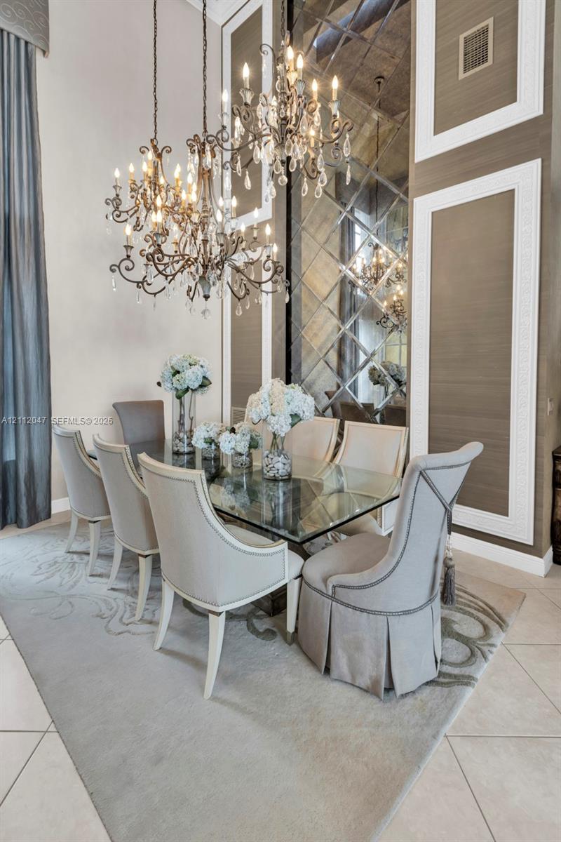 Dining area featuring dual iron-frame chandeliers, floor-to-ceiling mirror paneling with geometric lattice overlays, custom wall molding, and neutral-toned tile flooring