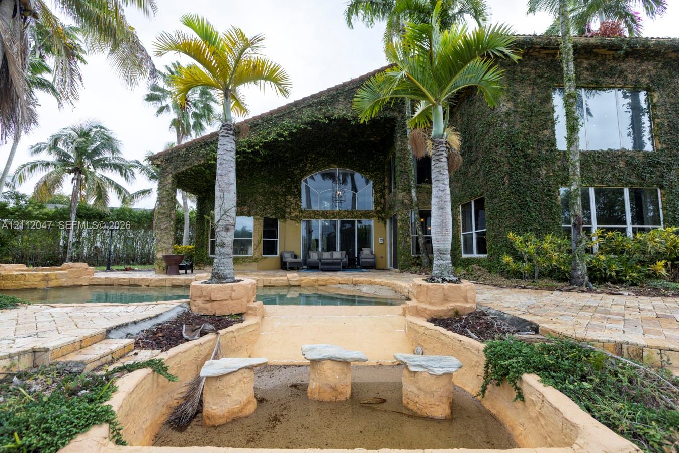 Two-story residence exterior featuring exterior wall vegetation, a stone-paved patio, an integrated swimming pool, and stone-accented palm tree planters