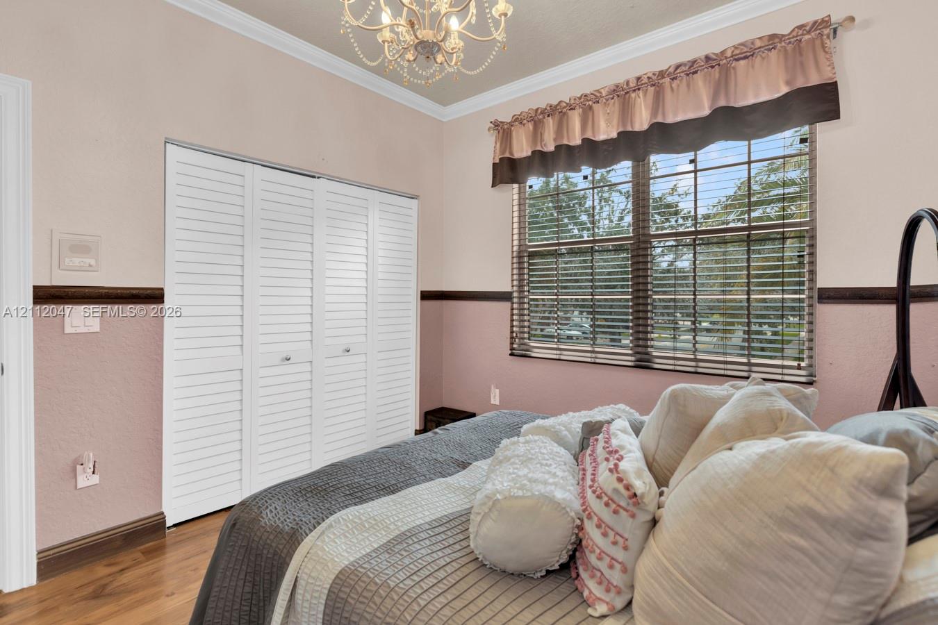 Room featuring wood-finish flooring, white louvered closet doors, a decorative ceiling chandelier, and a horizontal window with chair rail trim