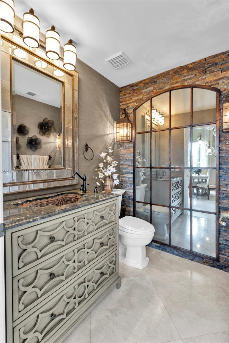 Custom vanity featuring decorative lattice-pattern cabinetry and a stone countertop, complemented by a floor-to-ceiling arched grid mirror, stacked stone accent wall, and multi-light vanity fixture