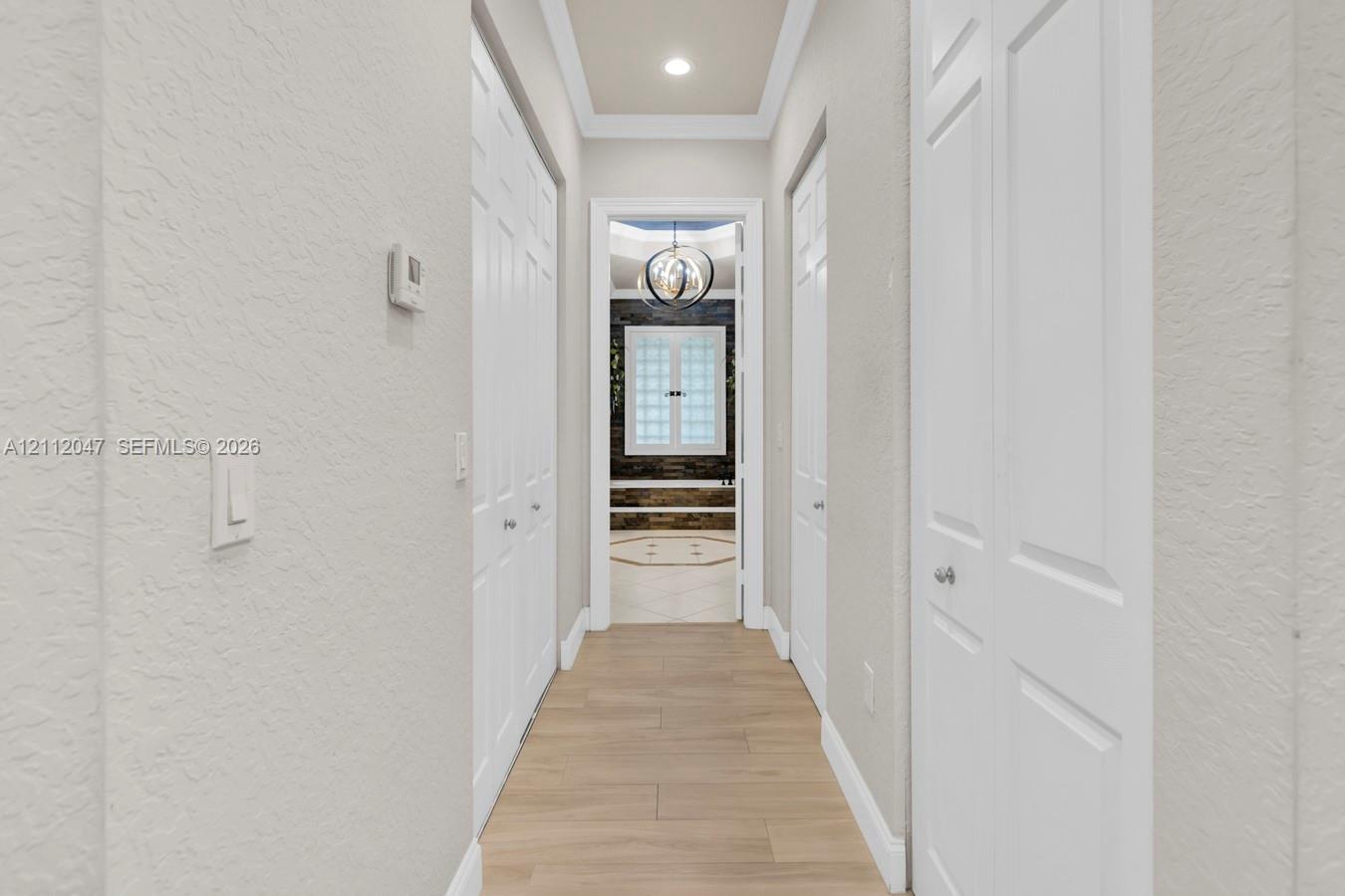 Hallway featuring wood-finish flooring, recessed ceiling lighting, crown molding, and double-door closets with chrome hardware