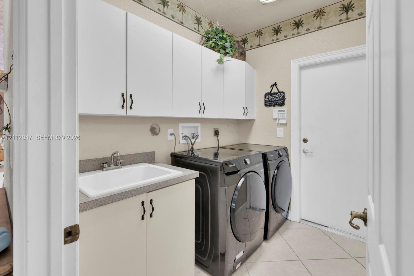 Laundry room featuring white wall-mounted cabinetry, a stone-finish countertop with an integrated utility sink, and tile flooring