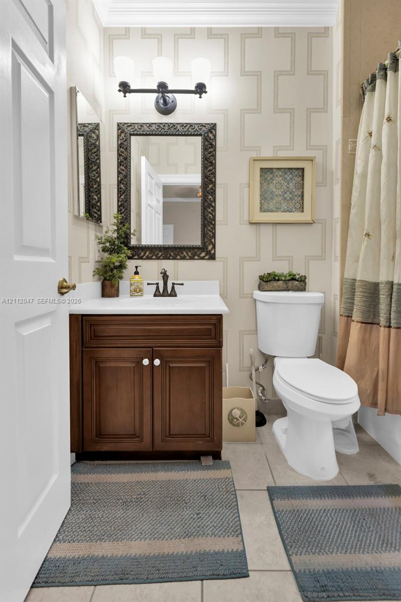 Bathroom featuring a dark wood-finish vanity with a white countertop, three-light vanity fixture, patterned wall covering, and tiled flooring