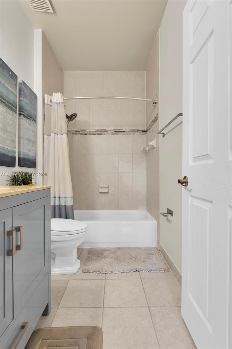 Bathroom featuring a gray vanity cabinet, tile flooring, bathtub with a tiled surround, integrated decorative tile inlay, and chrome hardware