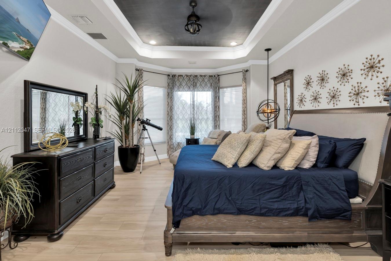Tray ceiling with dark finish, bay window, wood-finish flooring, and crown molding