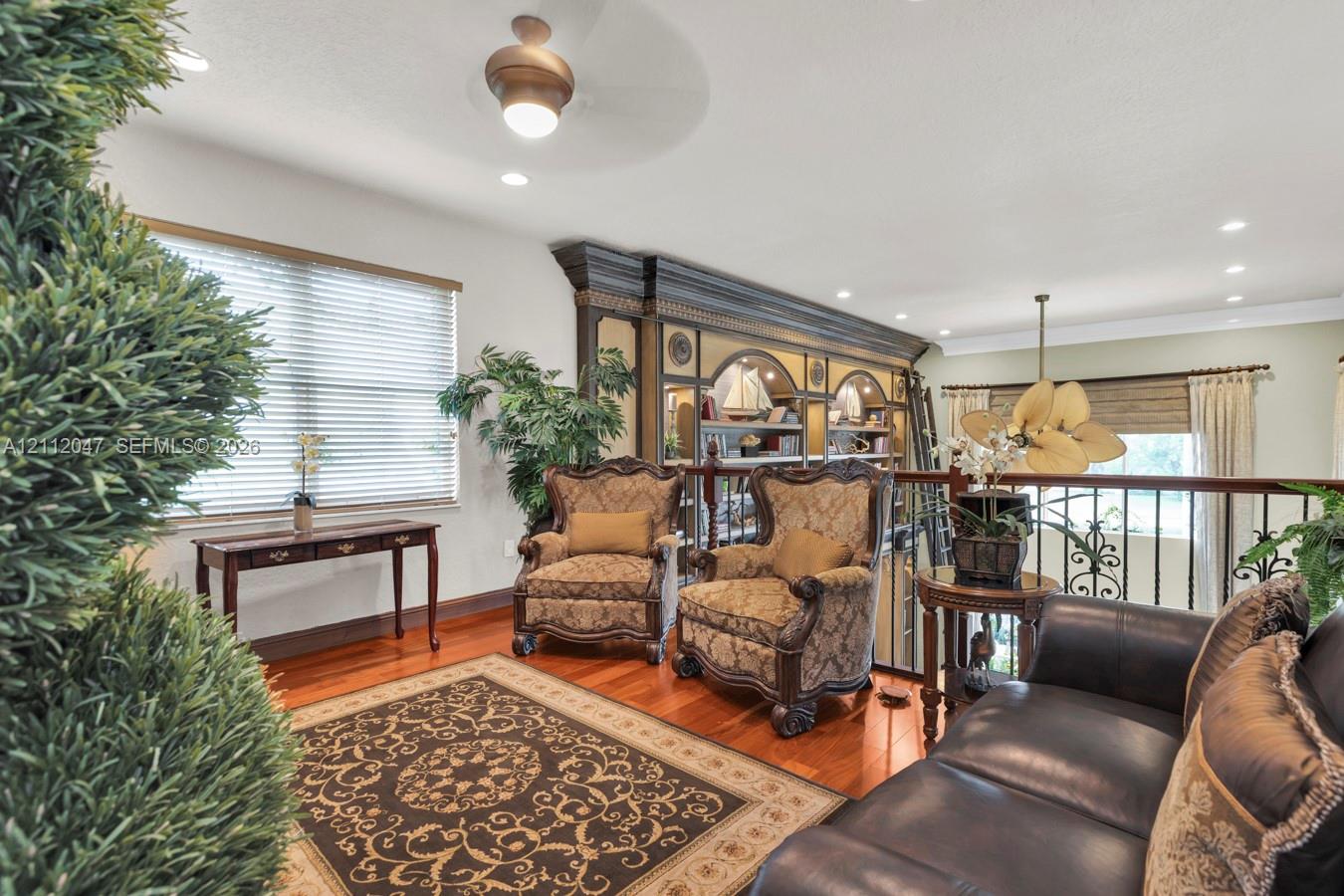 Built-in floor-to-ceiling wooden shelving with decorative arches, wood-finish flooring, recessed lighting, and ornate metal railing