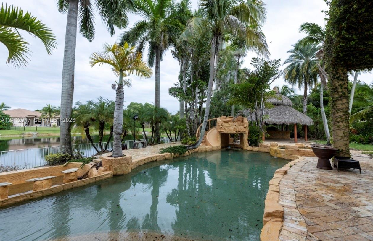 Custom pool featuring stone-style coping, a built-in slide, tiered rock formations, stone paver decking, and a thatched-roof tiki hut