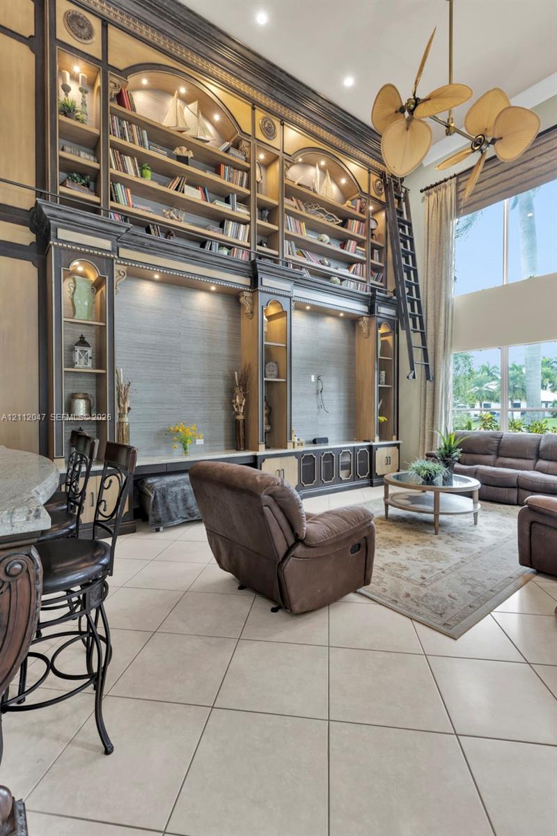 Floor-to-ceiling built-in cabinetry with integrated shelving and library ladder, vaulted ceilings, expansive windows, recessed lighting, and large-format tile flooring