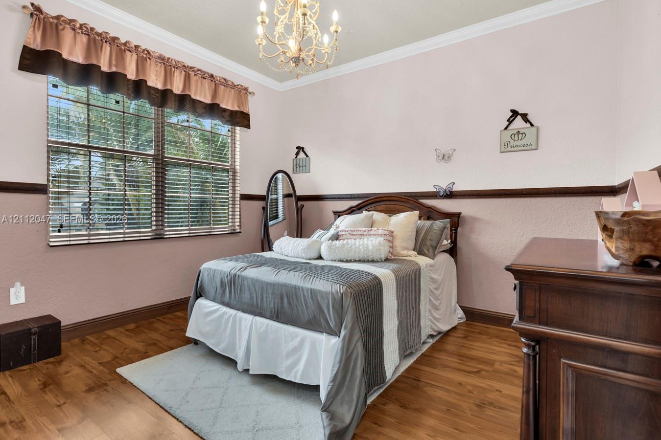 Room featuring wood-finish flooring, crown molding, two-tone wall paint with decorative chair rail, and an ornate multi-arm chandelier
