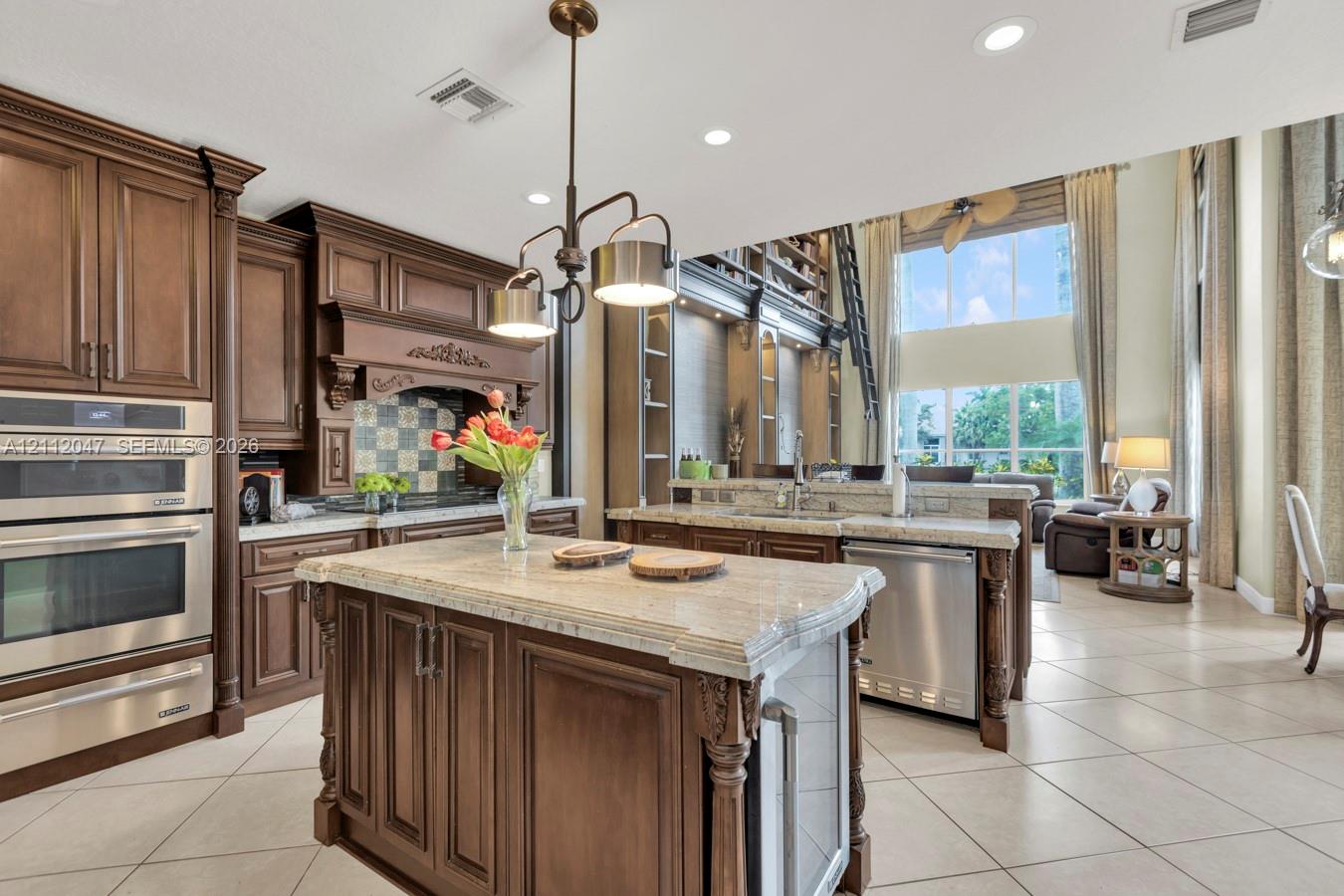 Kitchen featuring stained wood cabinetry, stone countertops, stainless steel double wall ovens, a central island with built-in storage, and tile flooring