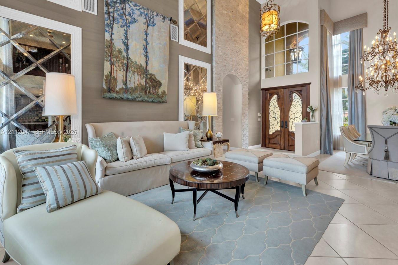 Two-story living area featuring a floor-to-ceiling stone fireplace, decorative mirrored wall panels, dual wrought-iron and wood entry doors, and an ornate multi-tiered crystal chandelier