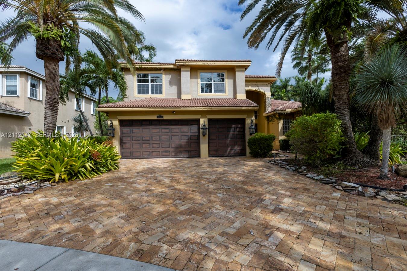 Two-story residence featuring a terracotta-tiled roof, herringbone-patterned paver driveway, double-car garage, and exterior wall sconces