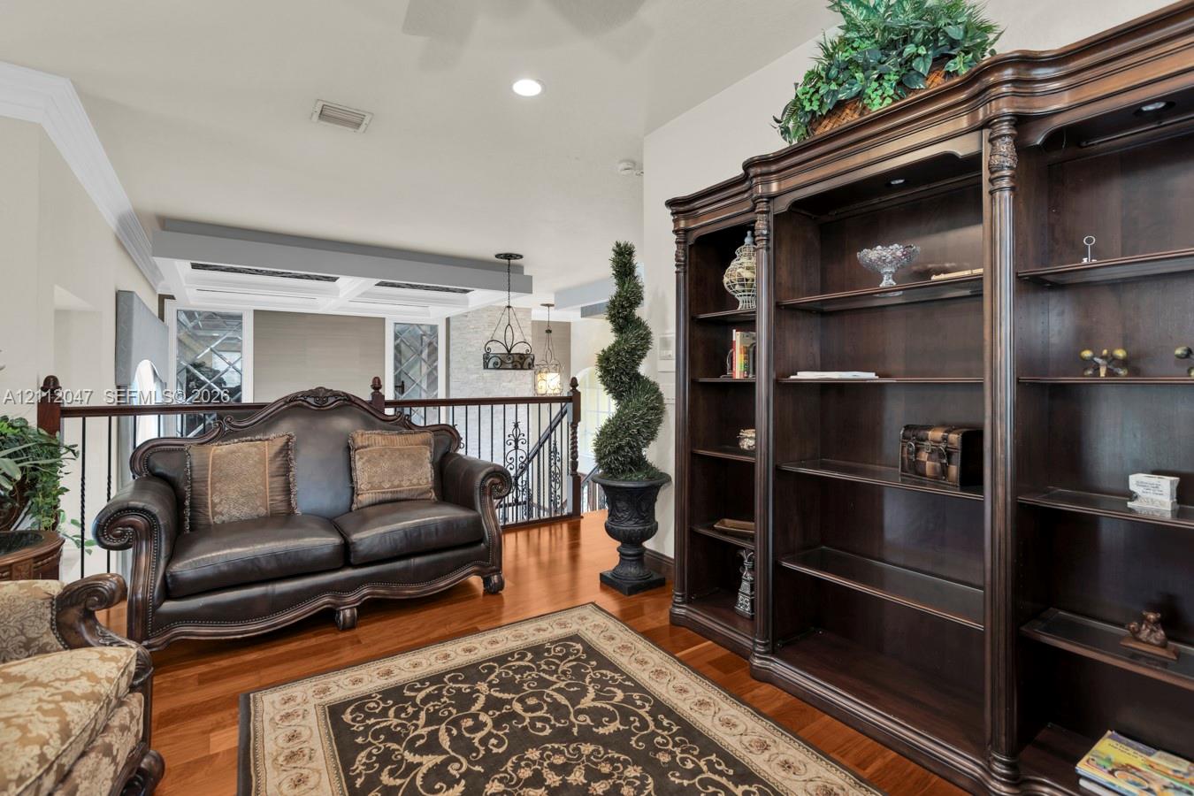 Built-in dark wood shelving unit with integrated lighting, wood-finish flooring, coffered ceiling detail, and metal stair railing