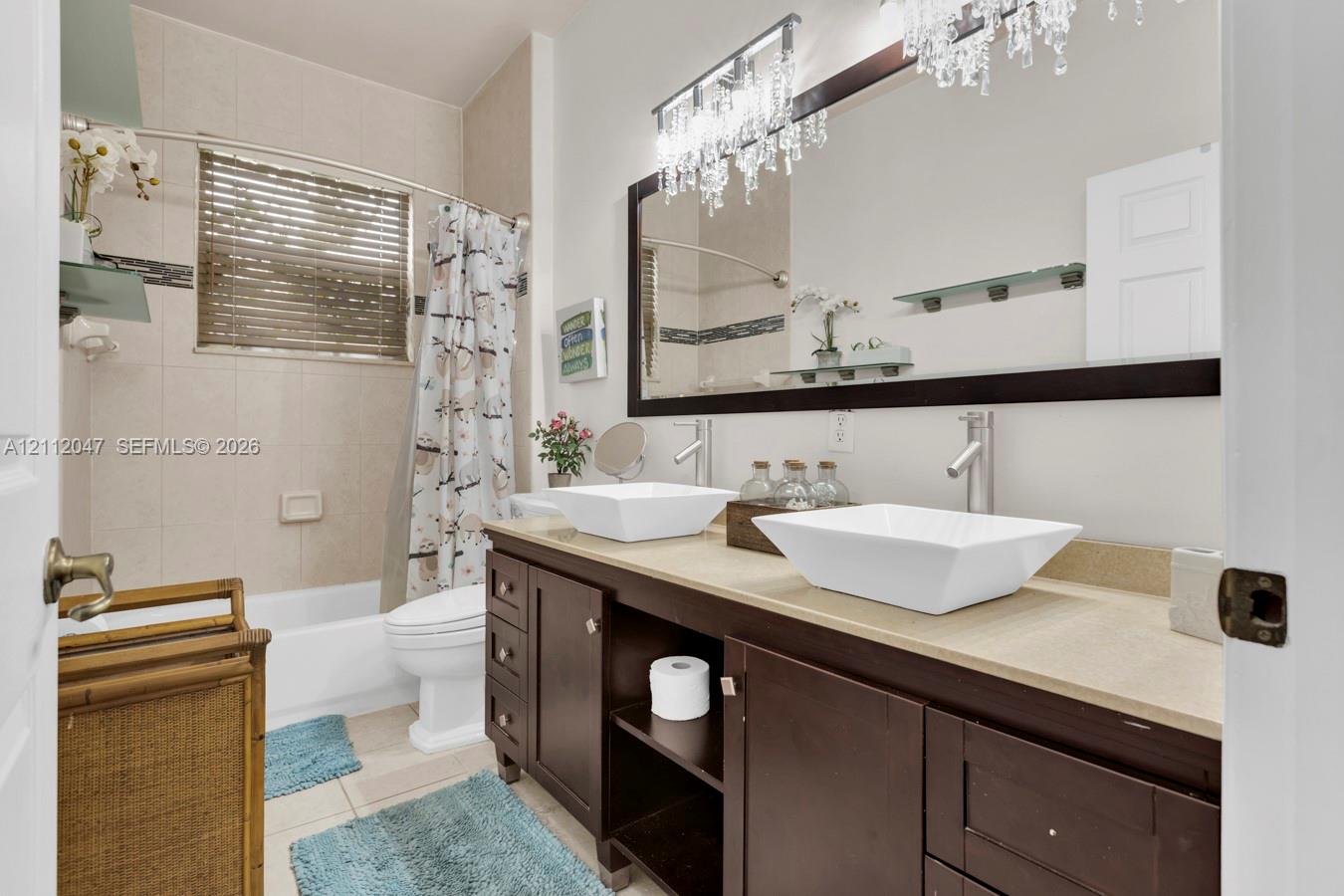 Double vanity featuring rectangular vessel sinks, dark wood cabinetry, a large framed mirror with integrated crystal lighting, and a neutral-toned tile shower surround