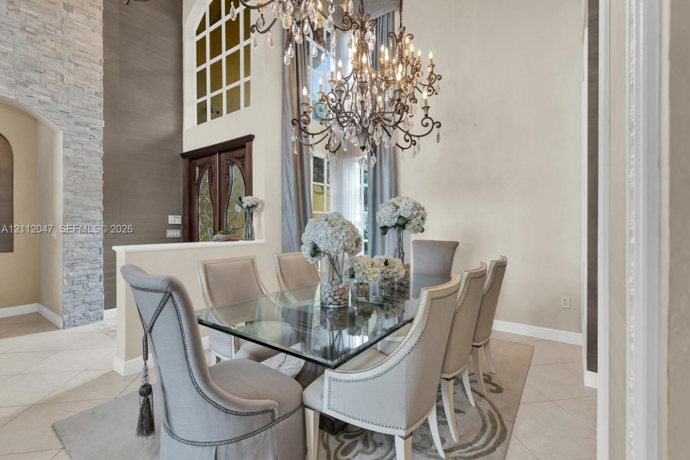 Double-height ceiling, floor-to-ceiling stone-textured wall feature, arched window with grid mullions, ornate tiered chandelier, and tile flooring