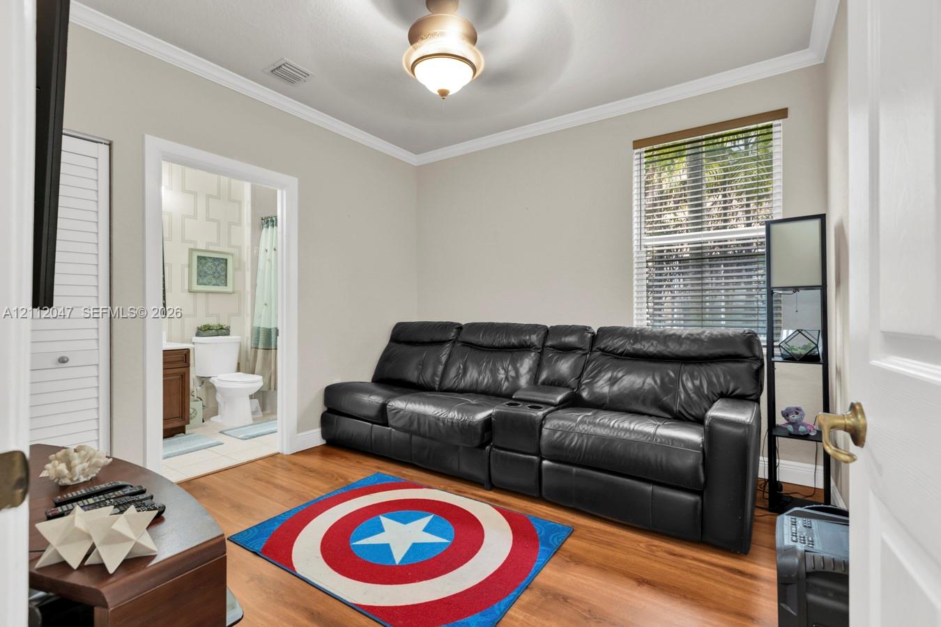 Room featuring wood-finish flooring, crown molding, a central ceiling-mounted light fixture, and a window with horizontal blinds