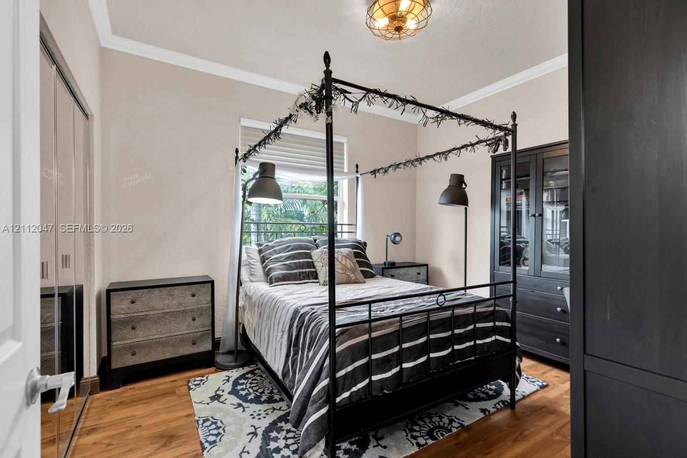 Wood-finish flooring, crown molding, double-door mirrored closet, and industrial-style flush-mount ceiling lighting