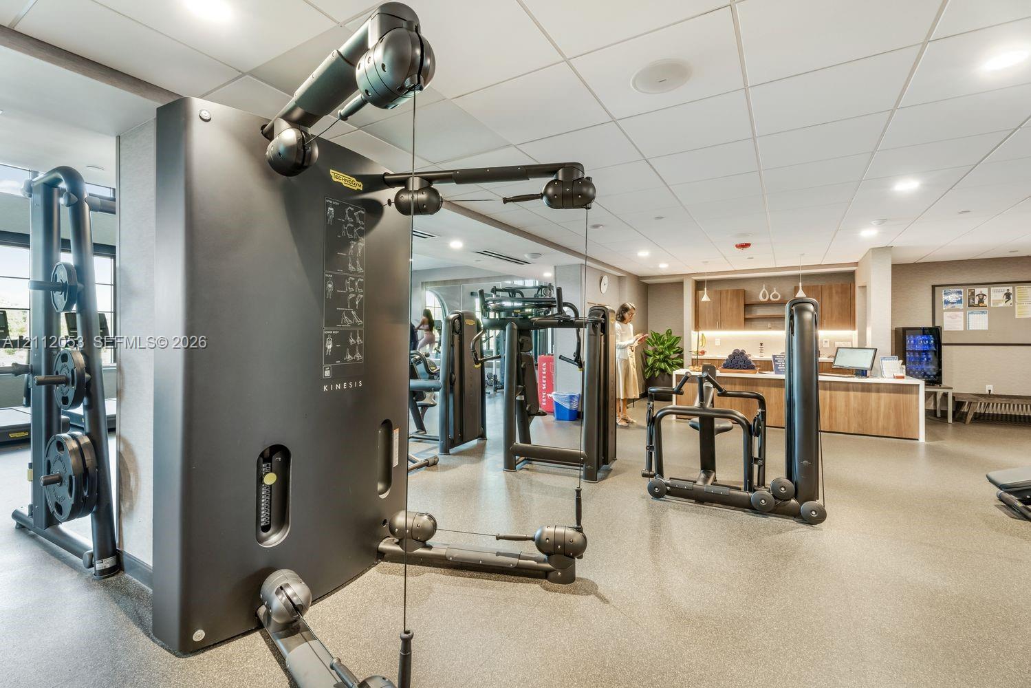 Fitness facility featuring professional-grade strength training equipment, recessed ceiling lighting, and a built-in refreshment station with wood-finish cabinetry