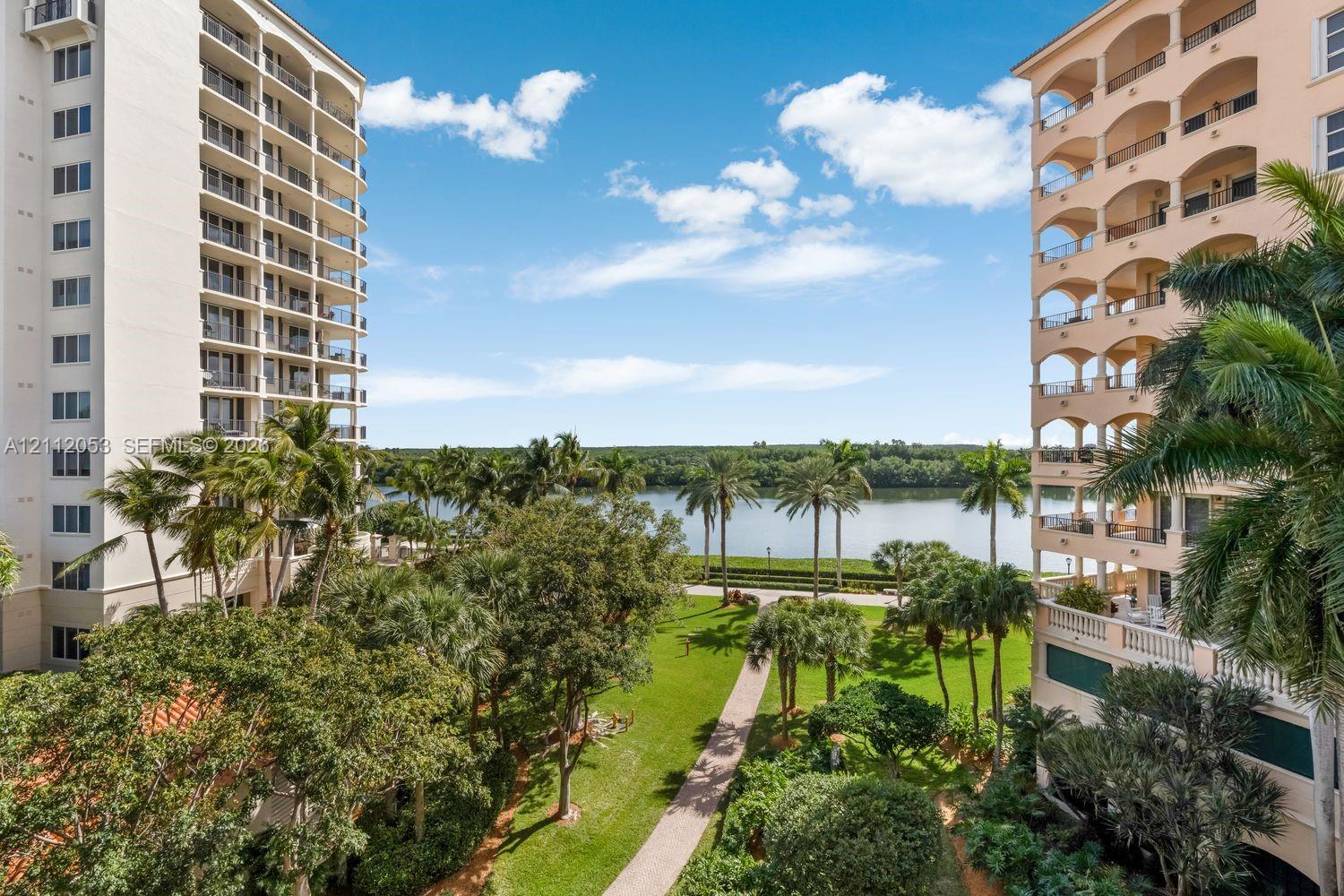 High-rise residential exterior featuring stacked arched balconies, manicured lawn, paved walkways, and palm tree landscaping