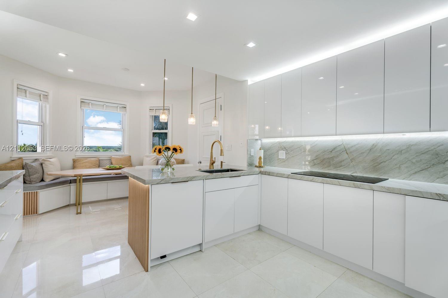 Kitchen featuring white flat-panel cabinetry, stone-finish countertops with matching backsplash, wood-accented island, built-in window seating, and recessed lighting