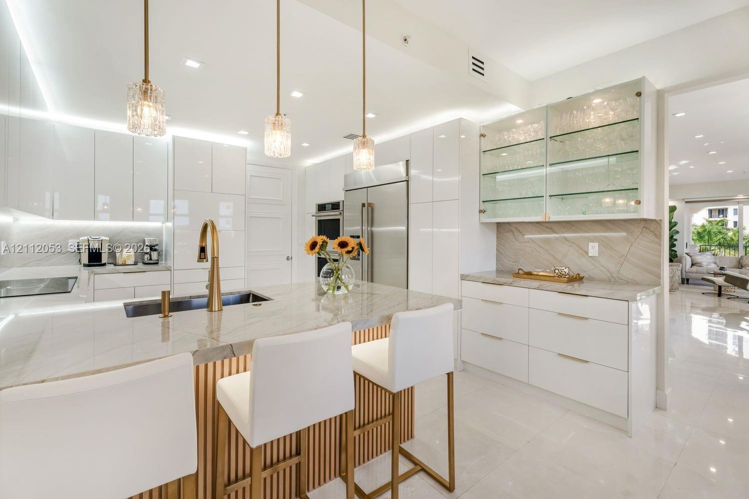 Modern kitchen featuring high-gloss cabinetry, stone-surface countertops, a center island with slat detailing, glass-front display shelving, and brass-finish hardware