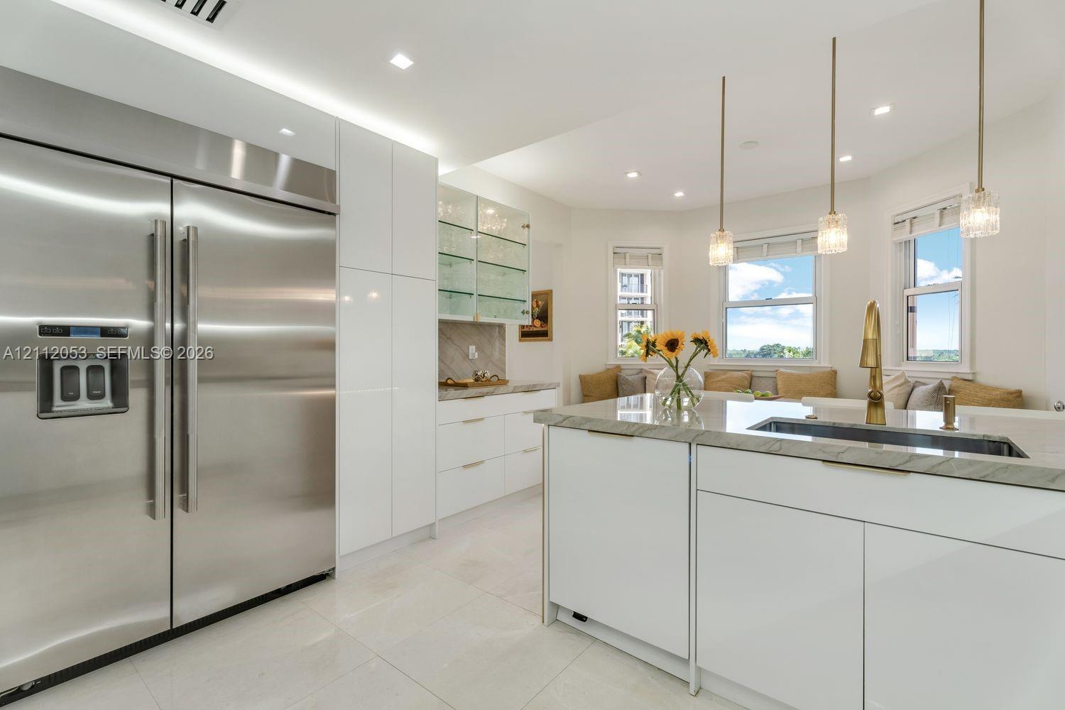 Kitchen featuring high-gloss white cabinetry, stainless steel side-by-side refrigerator, stone-topped island with a metallic faucet, and glass-front upper storage