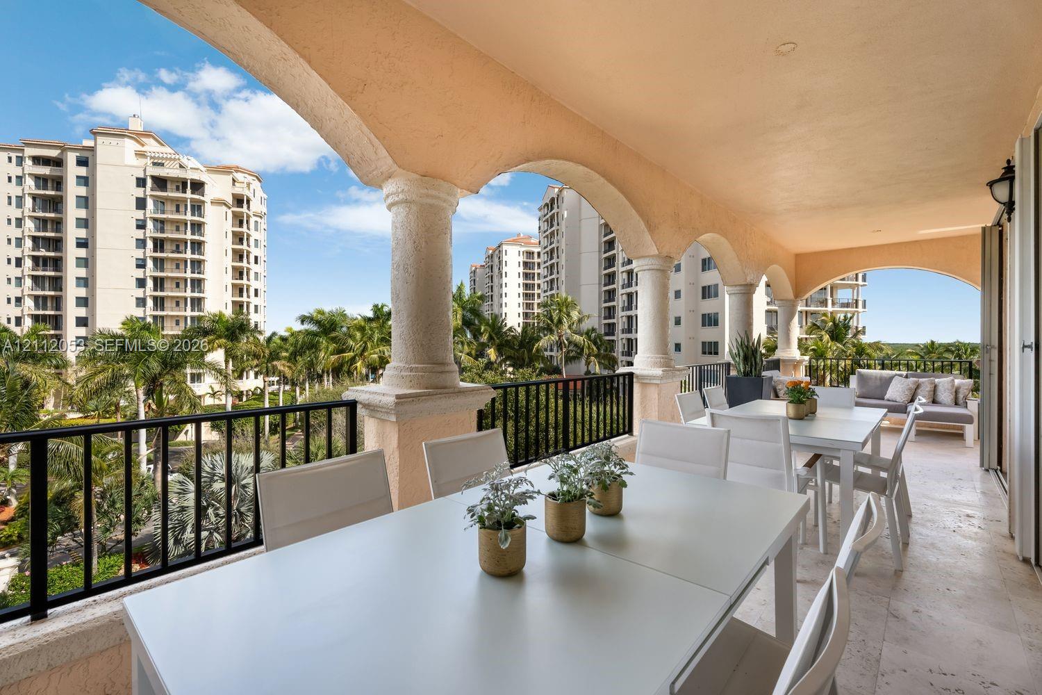 Covered balcony featuring stone-finish flooring, stucco-finished arches, textured structural columns, and black metal railings Covered balcony featuring stone-finish flooring, stucco-finished arches, textured structural columns, and black metal railings