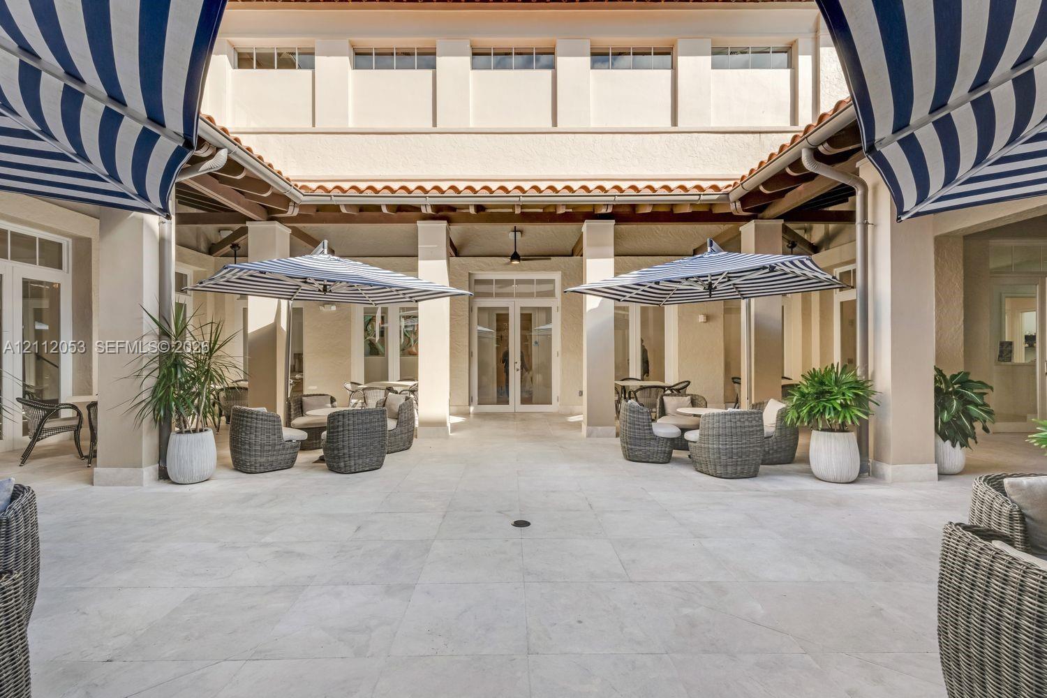 Enclosed courtyard featuring expansive stone tile flooring, covered loggia with exposed wood beam ceiling, structural pillars, and multi-pane glass double doors