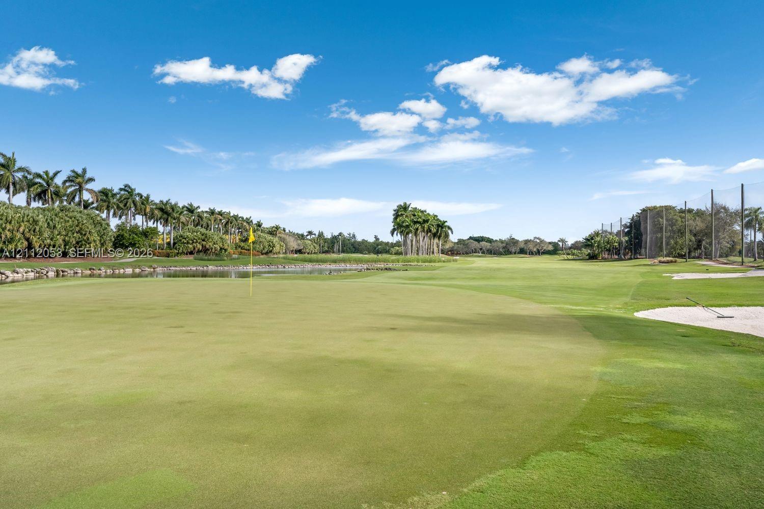 Golf course grounds featuring a manicured putting green, sand bunker, water hazard, and mature palm trees