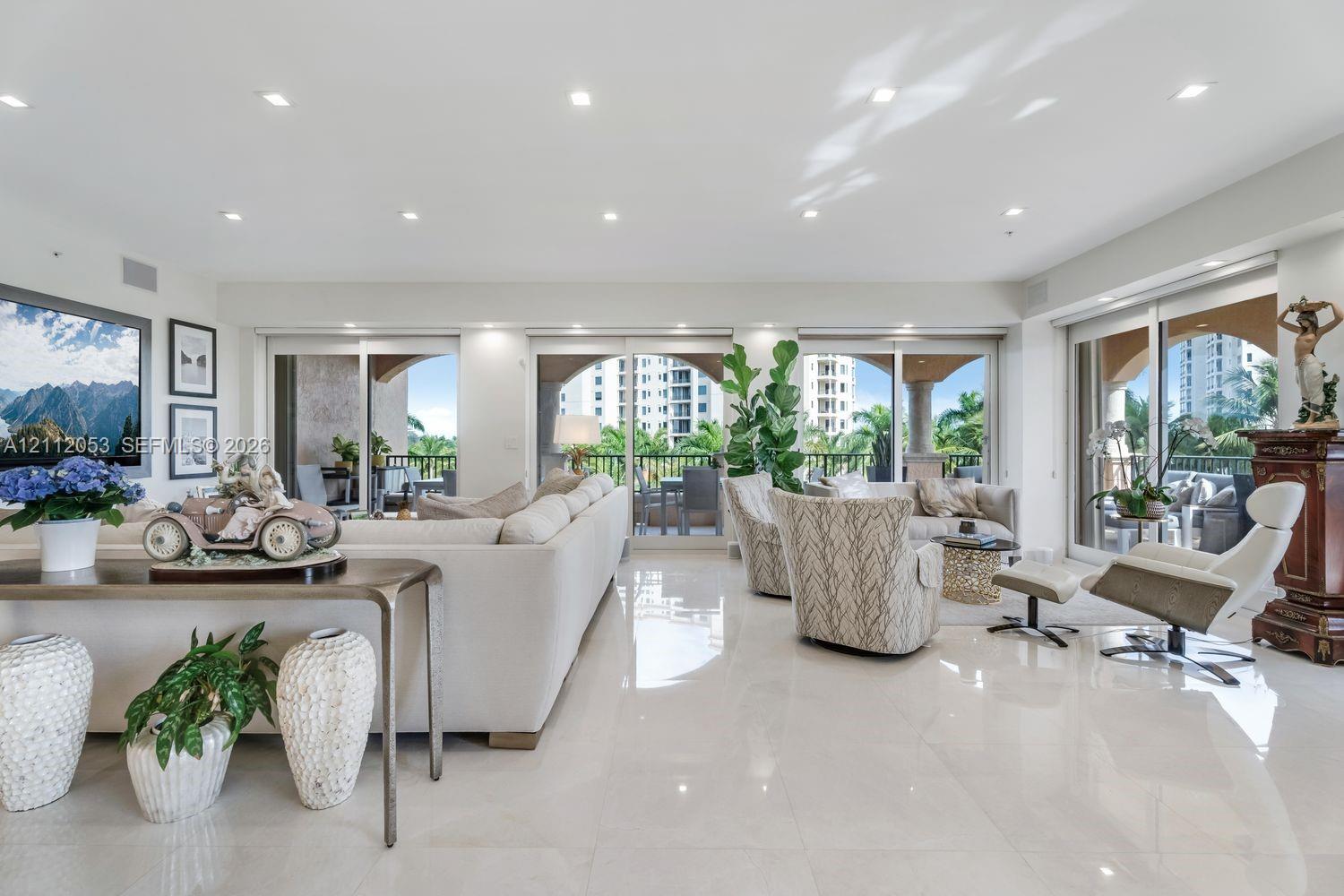 Open-concept living space featuring high-gloss tile flooring, recessed lighting, and expansive floor-to-ceiling glass sliding doors providing access to a covered balcony Open-concept living space featuring high-gloss tile flooring, recessed lighting, and expansive floor-to-ceiling glass sliding doors providing access to a covered balcony
