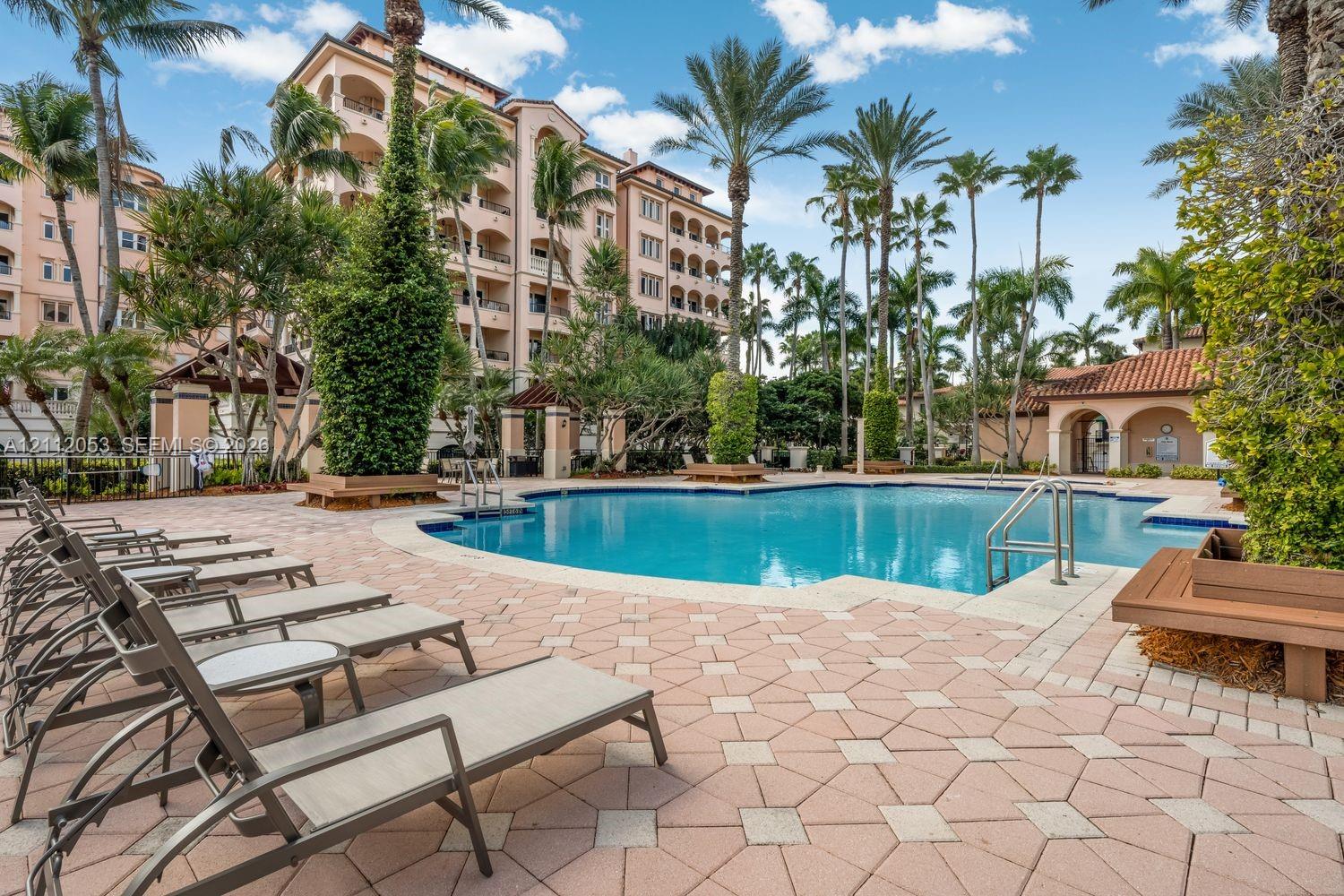Swimming pool area featuring a paved deck, built-in wooden bench seating, and mature landscaping