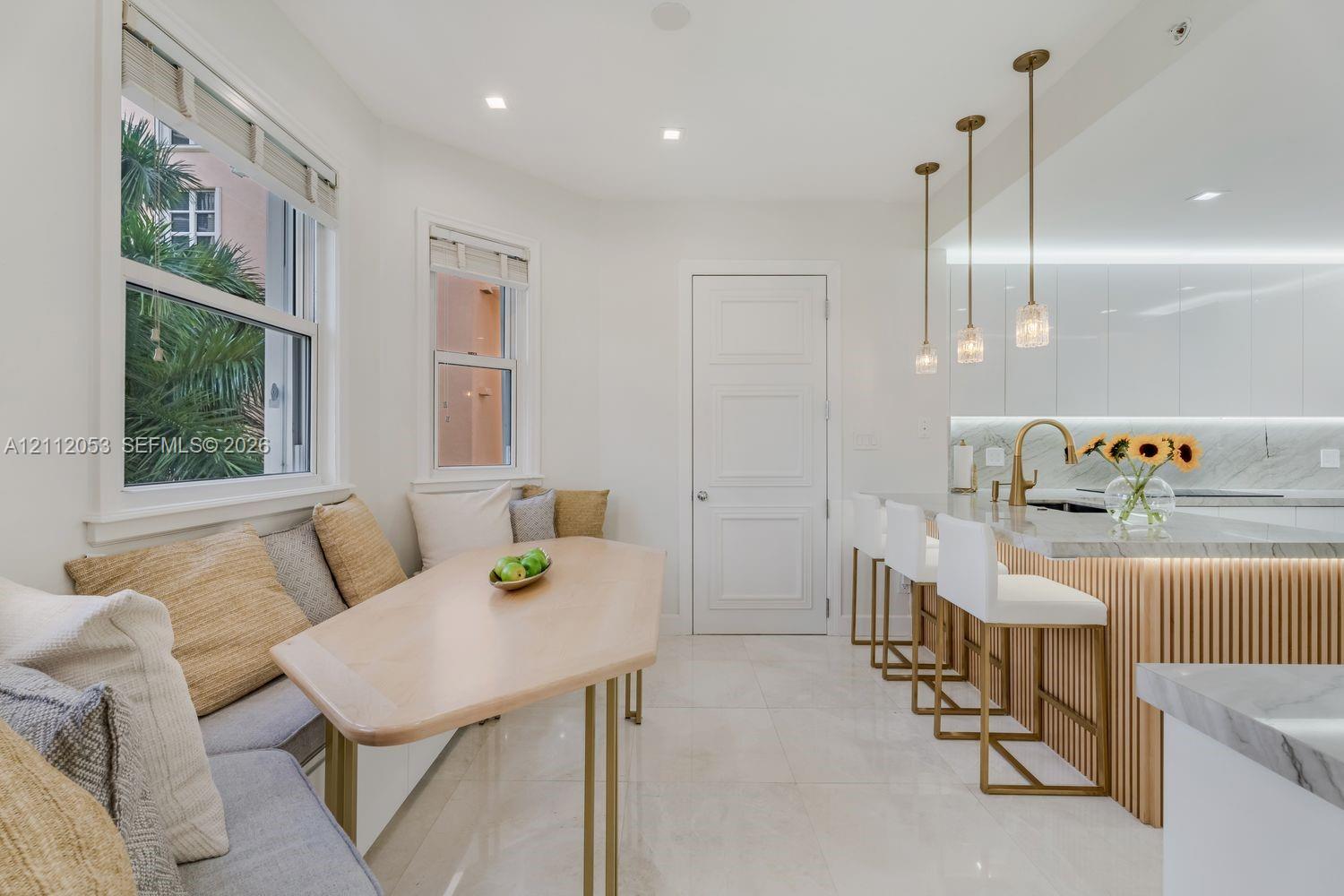 Kitchen featuring high-gloss cabinetry, stone-finish countertops, vertical wood-slat island detailing, brass-tone pendant lighting, and built-in bench seating