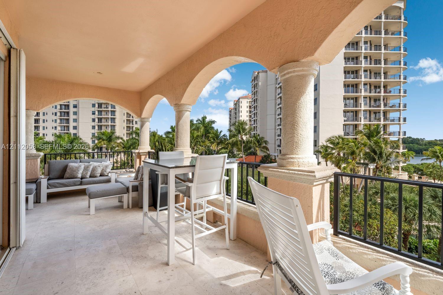 Covered balcony featuring arched stucco openings, decorative columns, stone-finish flooring, and black metal railings Covered balcony featuring arched stucco openings, decorative columns, stone-finish flooring, and black metal railings