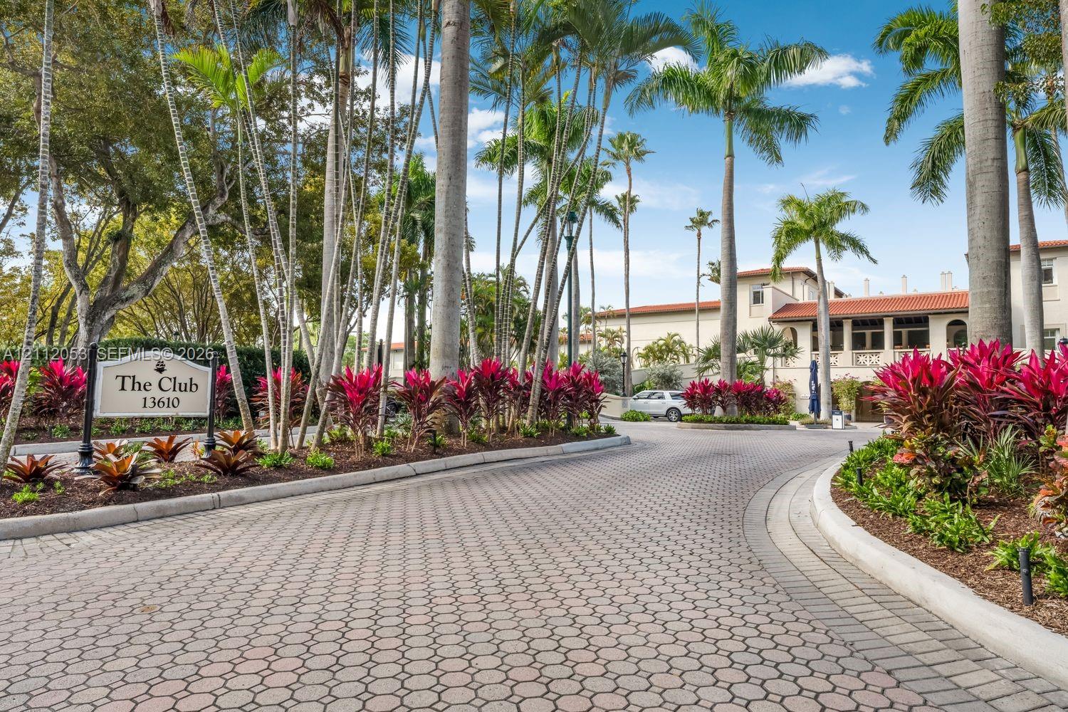 Paved stone driveway featuring mature palm trees, professional tropical landscaping, and a detailed entrance monument