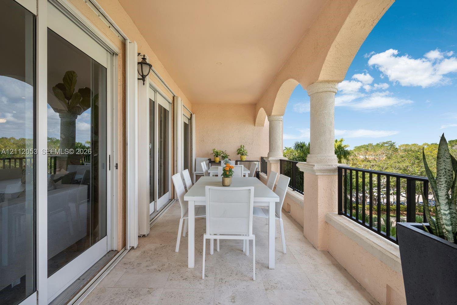 Covered balcony featuring stone tile flooring, arched structural columns, and black metal railings Covered balcony featuring stone tile flooring, arched structural columns, and black metal railings