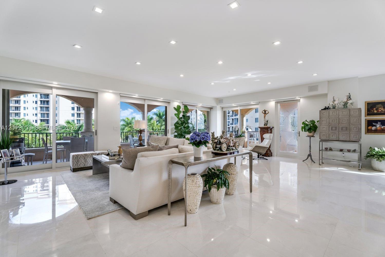 Spacious living area featuring polished stone flooring, recessed lighting, and multiple sliding glass doors providing access to a covered balcony Spacious living area featuring polished stone flooring, recessed lighting, and multiple sliding glass doors providing access to a covered balcony