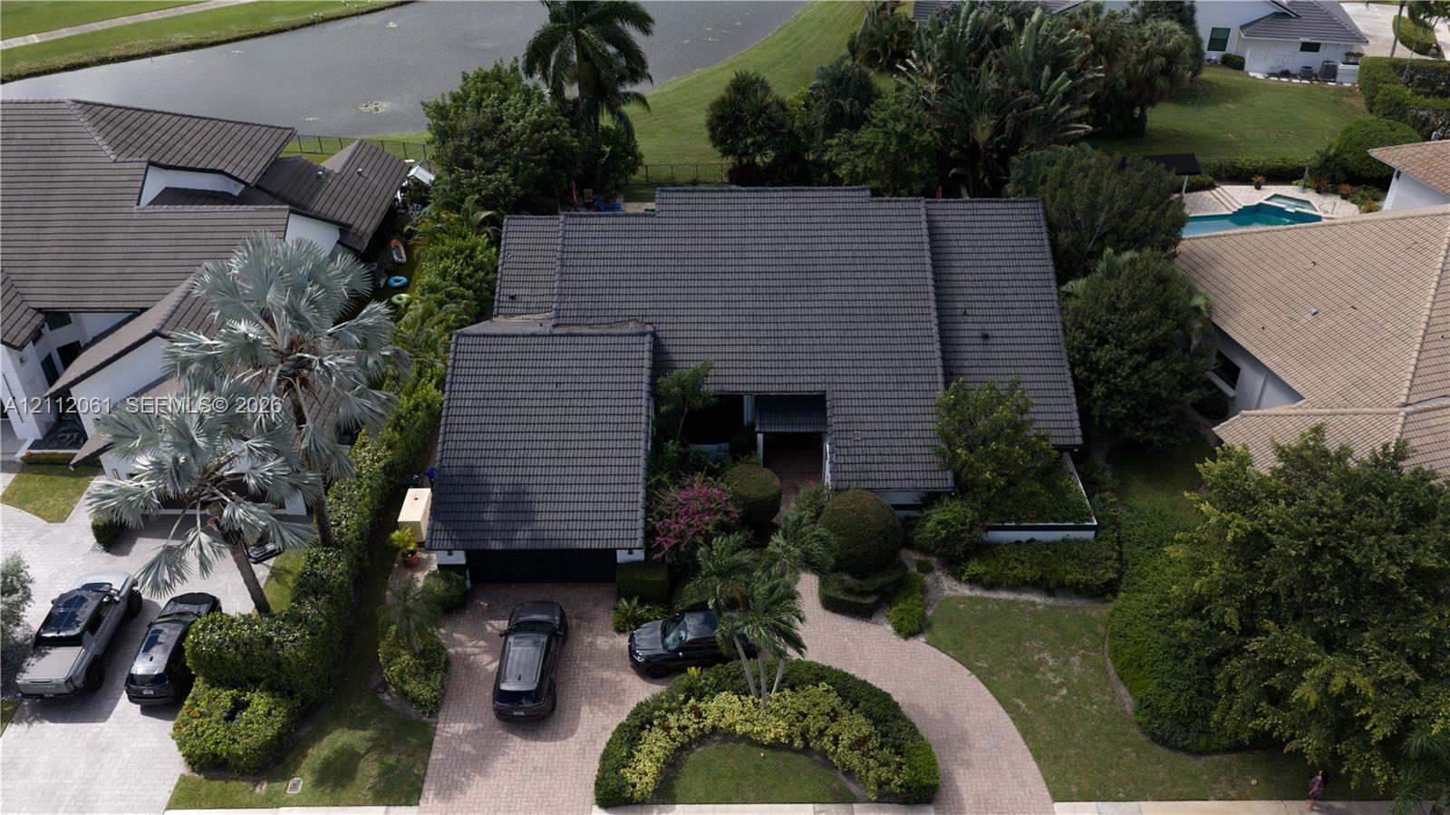 Aerial perspective featuring a multi-gabled tiled roof, paver driveway, and landscaped front grounds with mature palm trees Aerial perspective featuring a multi-gabled tiled roof, paver driveway, and landscaped front grounds with mature palm trees