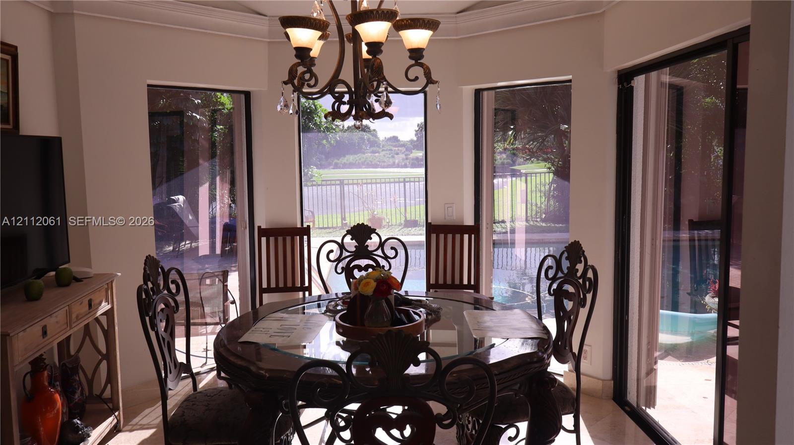 Octagonal-shaped breakfast area featuring large floor-to-ceiling windows, crown molding, a multi-arm metal chandelier, and sliding glass doors leading to the exterior