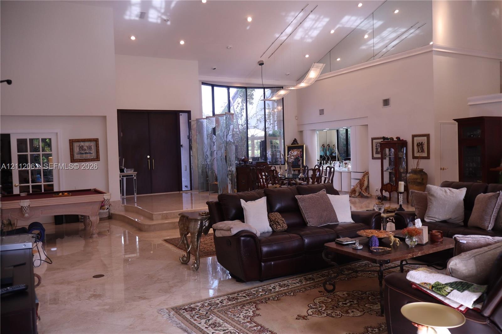 Vaulted ceilings with recessed lighting, polished stone flooring, floor-to-ceiling windows, raised entry platform, and a decorative glass privacy screen