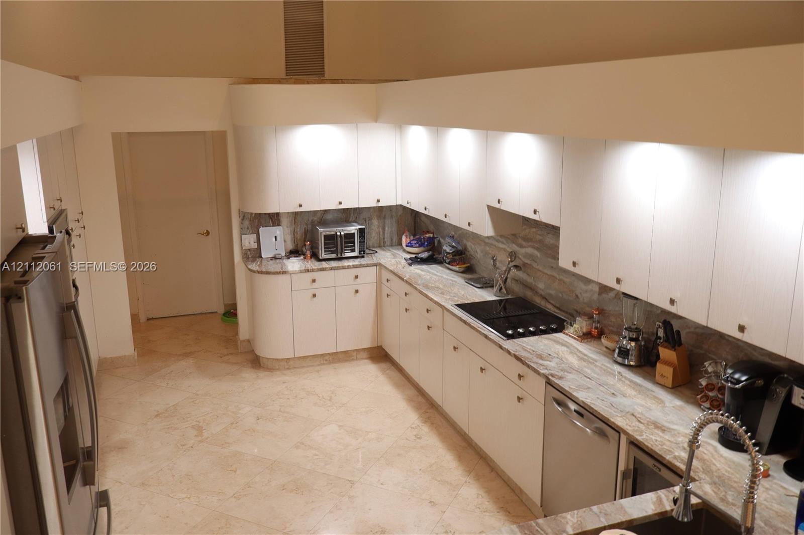Kitchen featuring light wood laminate cabinetry, pull out pantry ,solid marble countertops, matching marble backsplash, stainless steel appliances, and 24" marble flooring, dramatic high ceilings Kitchen featuring light wood laminate cabinetry, pull out pantry ,solid marble countertops, matching marble backsplash, stainless steel appliances, and 24" marble flooring, dramatic high ceilings