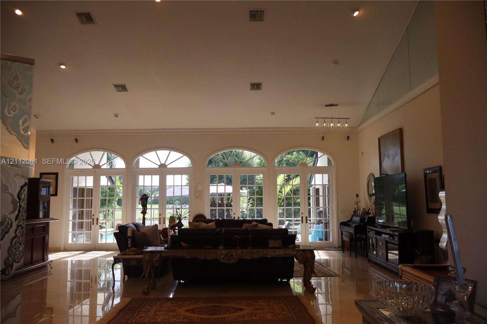High-ceiling interior featuring polished tile flooring, recessed lighting, and a series of four arched glass paneled double doors