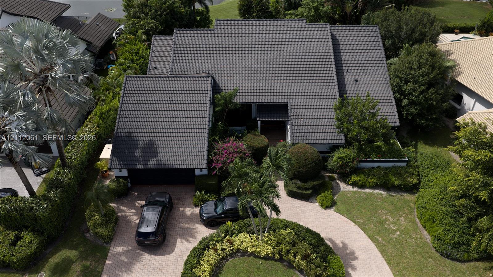 Aerial perspective featuring a multi-gabled tiled roof, paver circular driveway, and mature landscaping Aerial perspective featuring a multi-gabled tiled roof, paver circular driveway, and mature landscaping