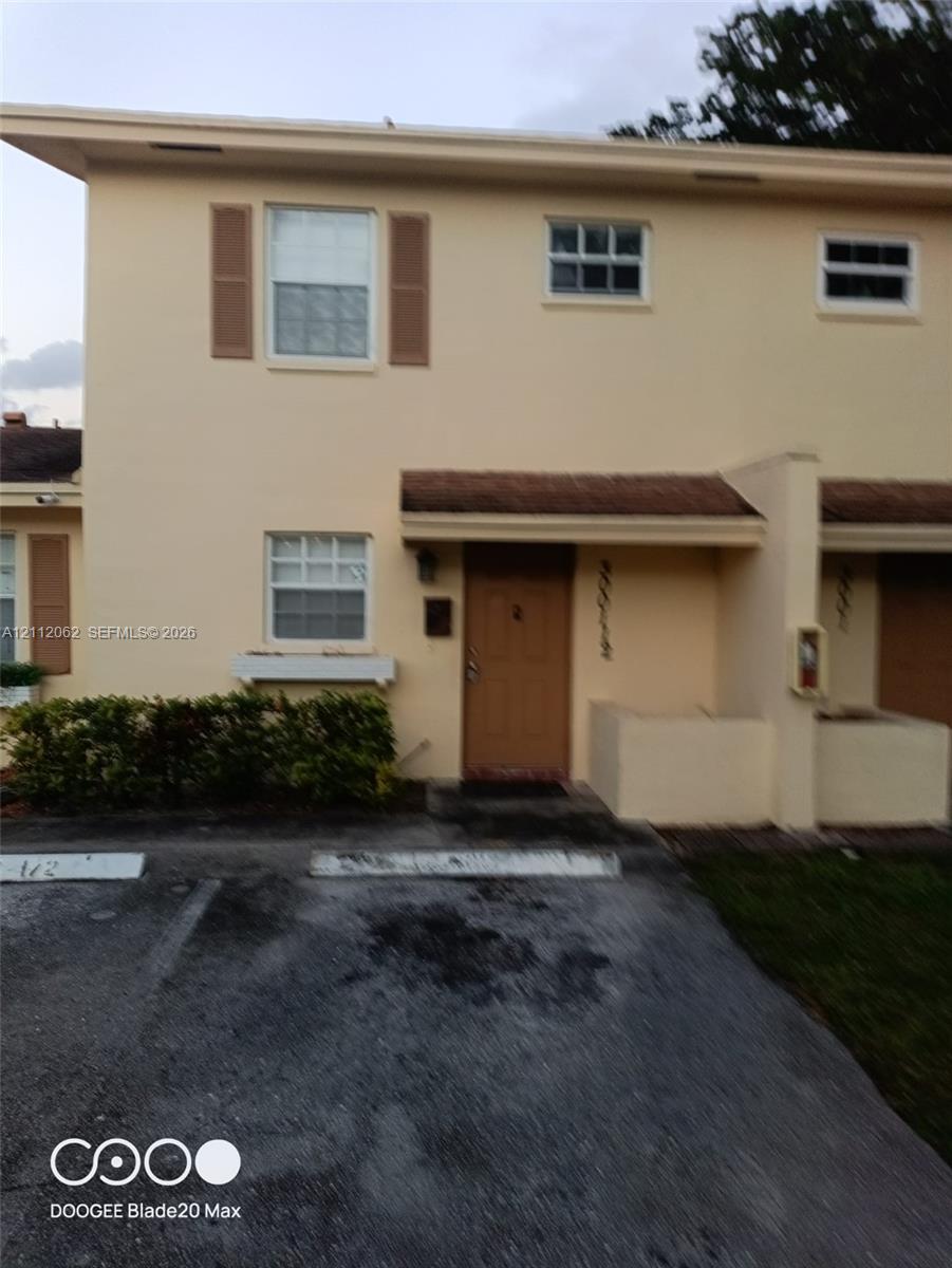 Two-story exterior featuring light-toned stucco facade, decorative window shutters, a covered entryway, and designated off-street parking