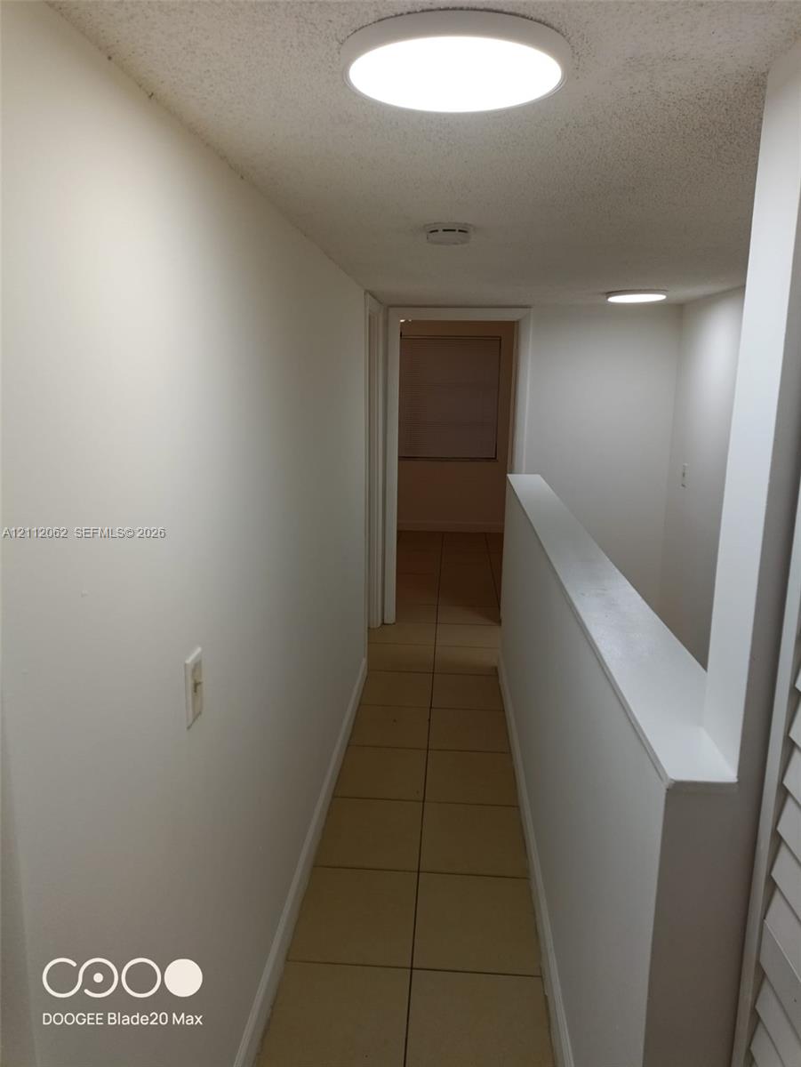 Neutral interior hallway featuring tile flooring, ceiling-mounted disc lighting, and crisp white wall finishes