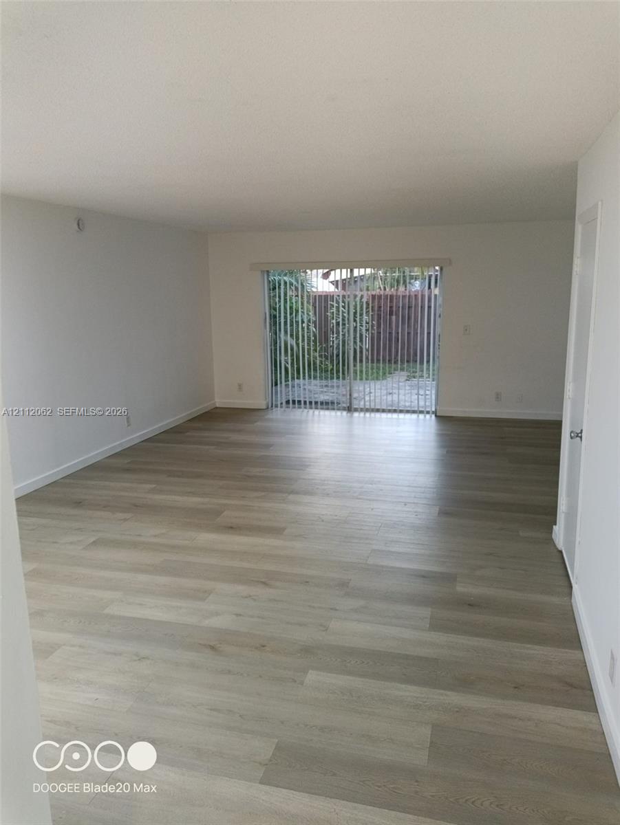 Open-concept interior featuring light-toned wood-finish flooring, neutral walls, and sliding glass doors with vertical blinds