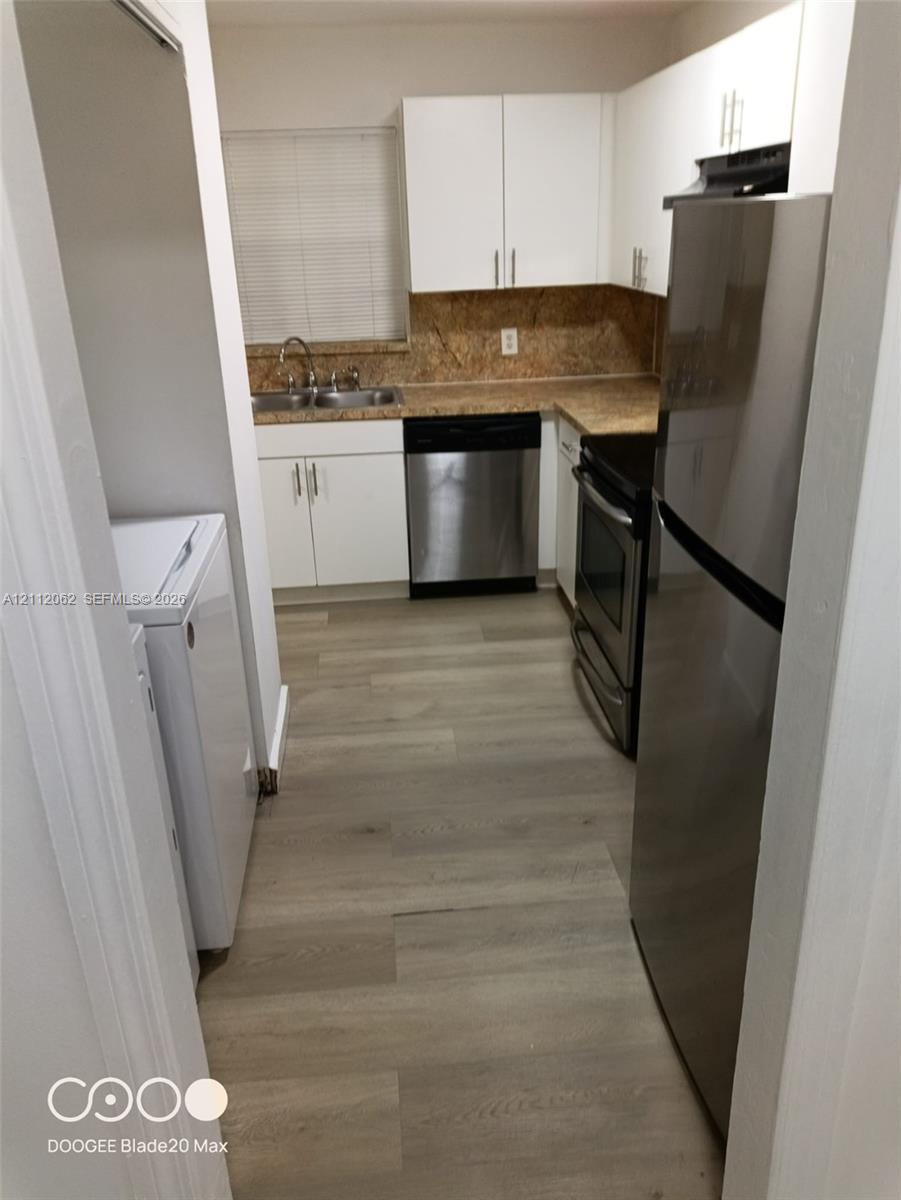 Kitchen featuring white cabinetry, wood-finish flooring, stainless steel appliances, and a dual-basin sink with a countertop