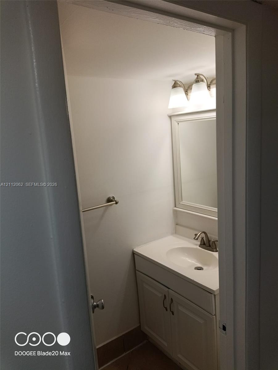 Vanity featuring a white cabinet, solid-surface countertop with an integrated oval sink, three-light fixture with white shades, wall-mounted mirror, and brushed-finish faucet