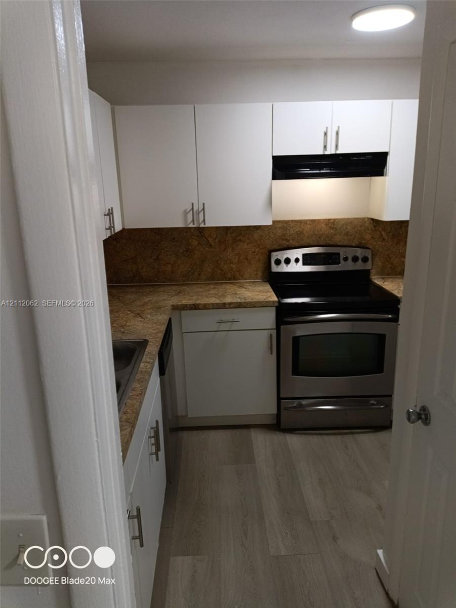 Kitchen featuring white cabinetry with brushed-metal pulls, stone-patterned countertops, stone-patterned backsplash, stainless steel range, and wood-finish flooring