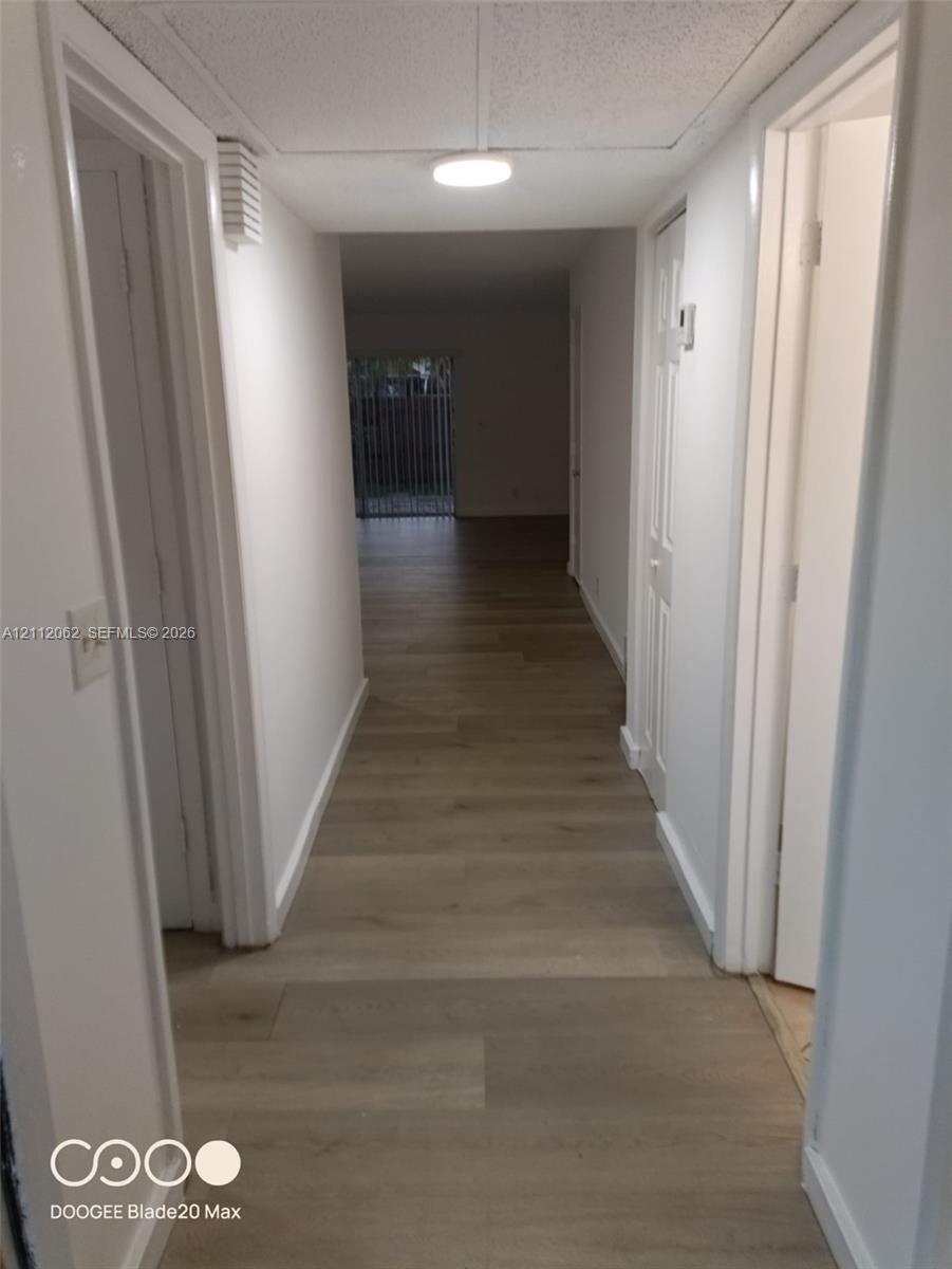 Hallway featuring wood-finish flooring, white paneled interior doors, and a ceiling-mounted light fixture