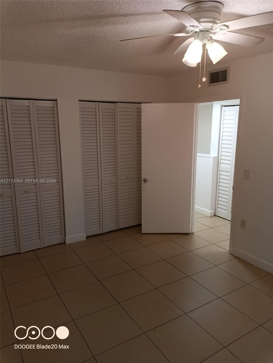 Room featuring neutral ceramic tile flooring, dual floor-to-ceiling closets with louvered bi-fold doors, and a ceiling fan with integrated lighting